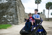 Toddler Rhett Natto, son of local U.S. Marine veteran Chris Natto, sits on his father’s lap to steer his new all-terrain wheelchair around the grounds of the Castillo de San Marcos on Wednesday, June 28 2017. Chris Natto, who was partially paralyzed in a parachute accident during a Feb. 2016 training exercise at Fort Bragg, was presented with the chair on Wednesday by Freedom Alliance, a national organization supporting American military veterans and their families. The chair is designed to provide Natto the mobility needed to more easily join his family in outdoor adventures, such as beach visits and trail walking. (Christina Kelso/ The St. Augustine Record)